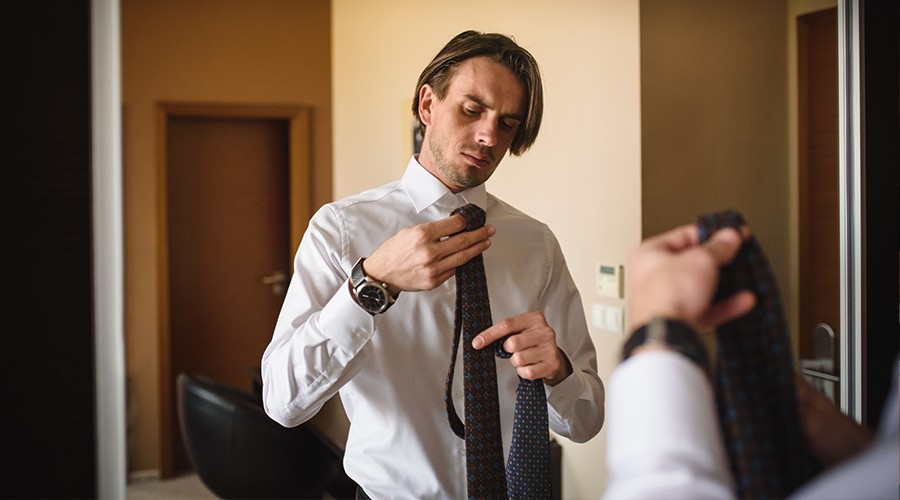 Odraz muže v zrcadle při vázání kravaty